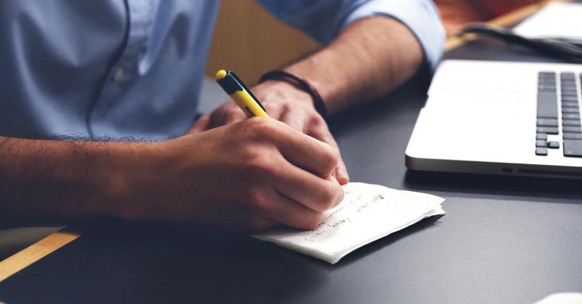 Person writing notes with notepad and pencil